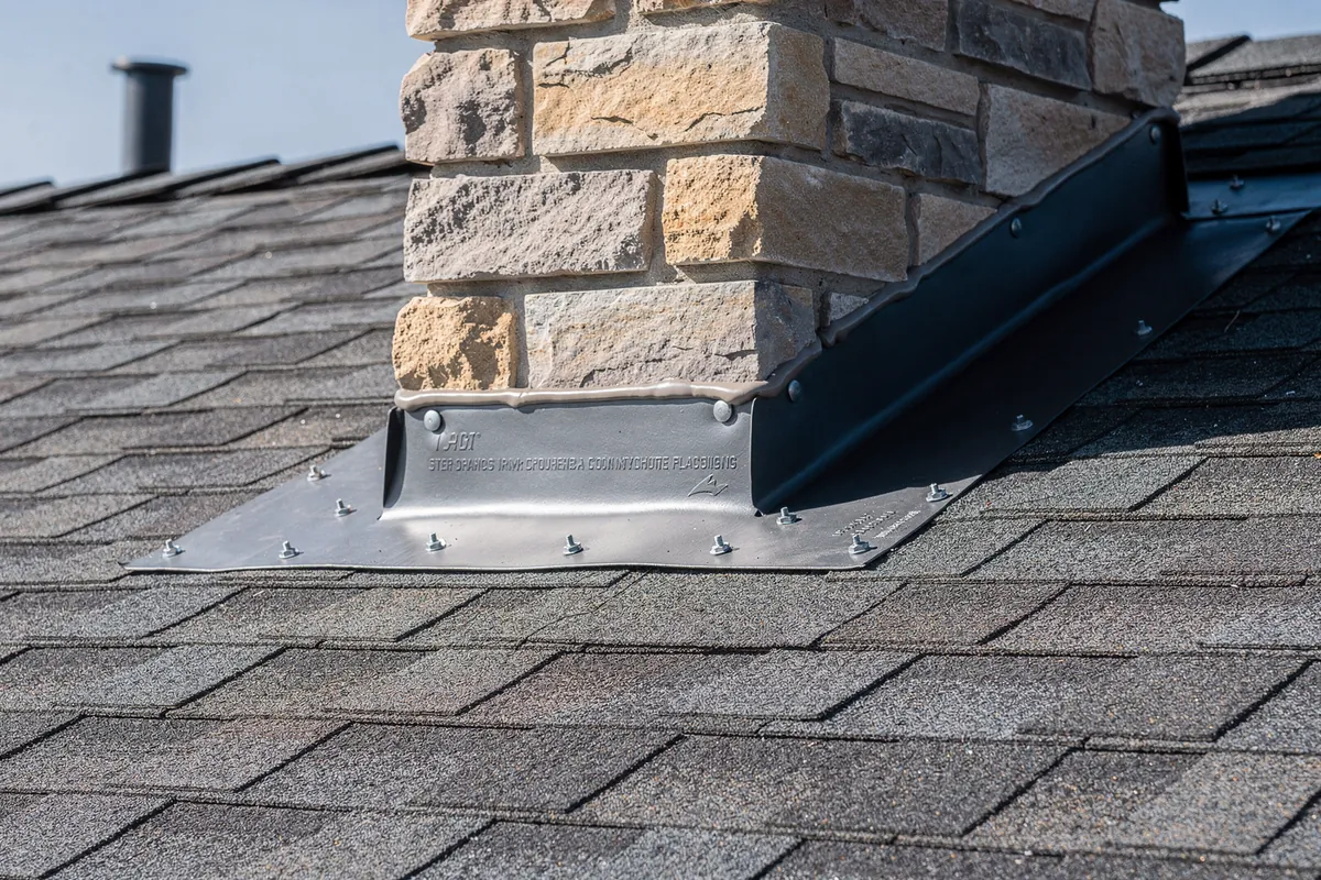 New step flashing where a shingle roof meets a stone chimney